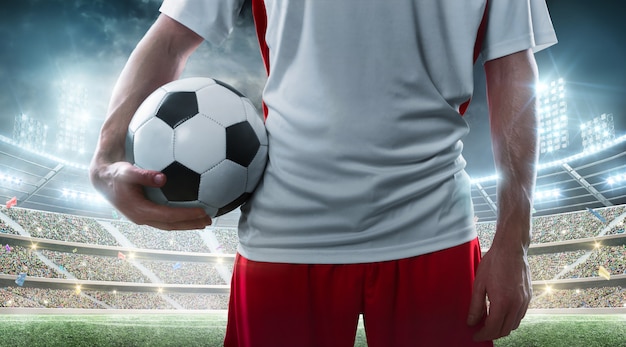 Sport. Professional soccer player holding soccer ball on the stadium. Close up