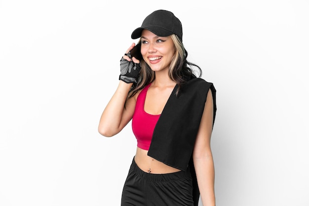 Спортивная русская девушка в шляпе и полотенце на белом фоне ведет разговор с мобильным телефоном