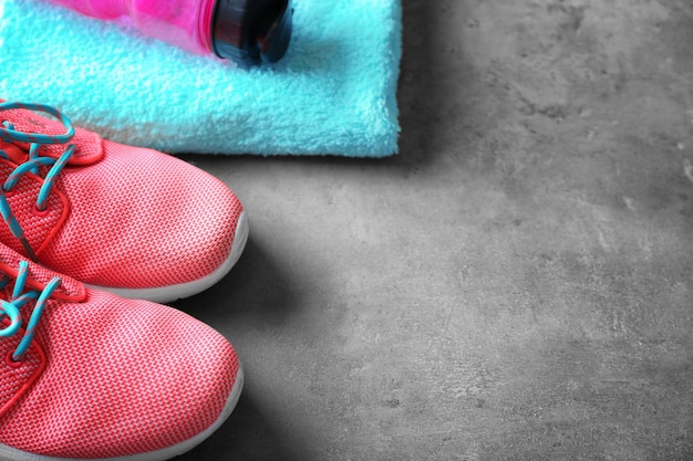 Sport shoes bottle of water and towel on grey table closeup