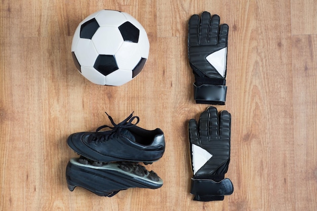 Photo sport, soccer, football and sports equipment concept - close up of ball, boots and goalkeeper gloves on wooden background