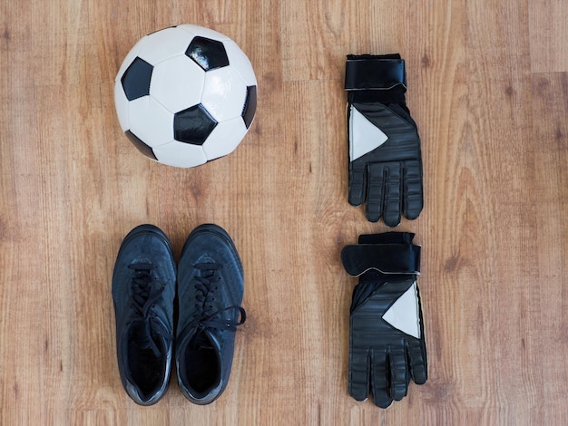 sport, soccer, football and sports equipment concept - close up of ball, boots and goalkeeper gloves on wooden background