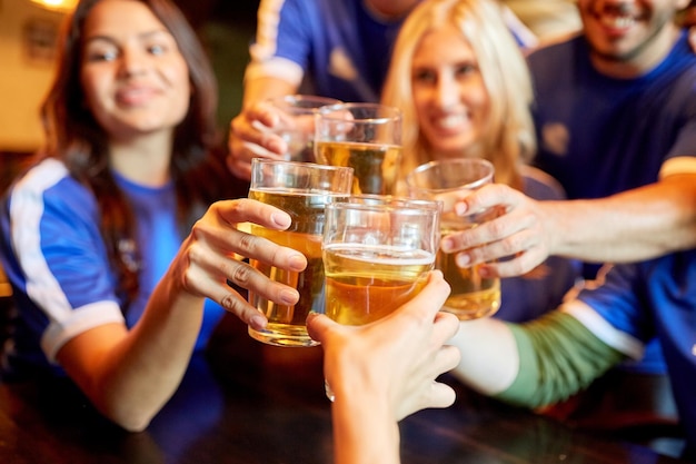 sport, soccer, people and leisure concept - happy friends or football fans clinking beer glasses at bar or pub