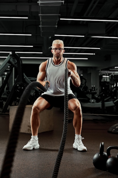 Sport. uomo forte che si esercita con corde da battaglia in palestra con atleta che fa allenamento con la corda di battaglia in palestra sfondo sportivo drammatico.