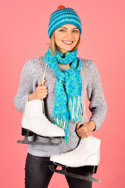 Sport style, winter fashion. smile woman skater with figure\
skates in hat, scarf and sweater. vacation, holidays, lifestyle -\
girl with ice skates getting ready for ice skating, winter sport\
activity.