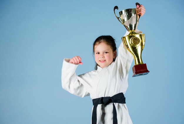 sport success in single combat. practicing Kung Fu. happy childhood. winner little girl in gi sportswear. small girl with champion cup. martial arts. energy and activity for kids. Striking the pose.