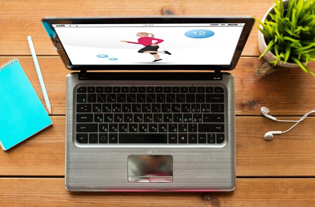 sport and technology concept - close up of laptop computer with fitness application on screen on wooden table