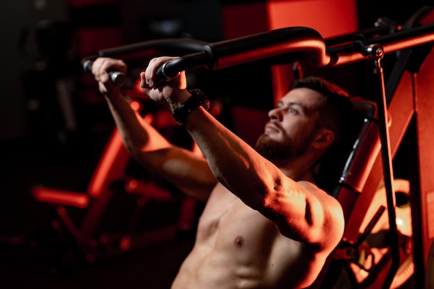 Photo sport, technology, lifestyle and people concept. young man with flexing chest muscles on gym equipment. view from the back.