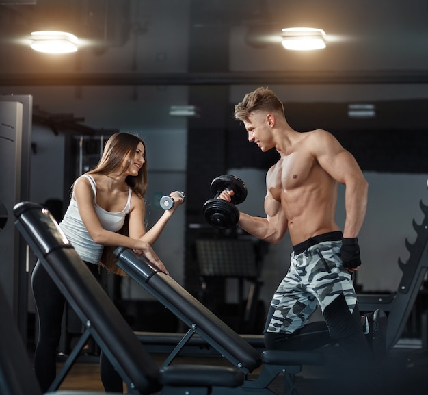 Sport, training, fitness, lifestyle and people concept - young woman with personal trainer flexing back and abdominal muscles on bench in gym. High quality photo