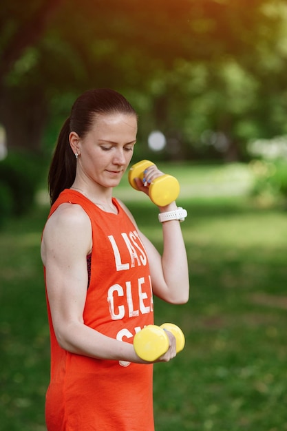 Sport trainingsconcept Het meisje houdt zich bezig met fitness in de natuur Zijaanzicht van een jonge vrouw die rekoefeningen doet met halters Actieve atleet die aan fitnessroutine werkt om af te vallen