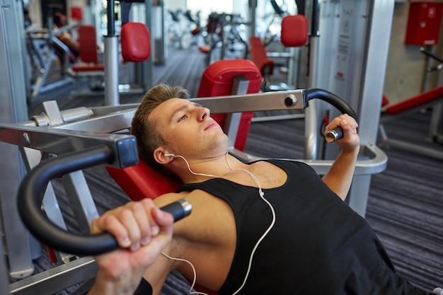 sport, uitrusting, technologie, levensstijl en mensenconcept - jonge man met koptelefoon die borstspieren buigt op gymmachine