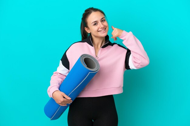 Sport Ukrainian woman going to yoga classes while holding a mat making phone gesture Call me back sign