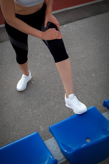 Спорт и хорошее самочувствие. Девушка фитнеса в белых кроссовках делает растяжку тренировки. Фасонируйте спортивную женщину с сильной тренировкой мускулистого тела. Подходящая женская растяжка на открытом стадионе