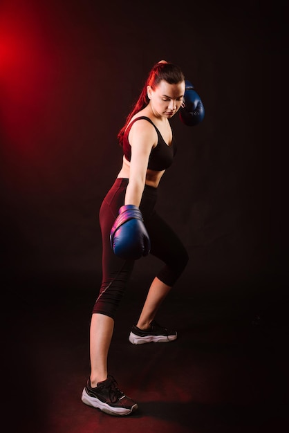 Sport woman boxer wearing blue boxing gloves on dark background