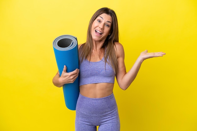 Sport woman going to yoga classes while holding a mat isolated non yellow background with shocked facial expression