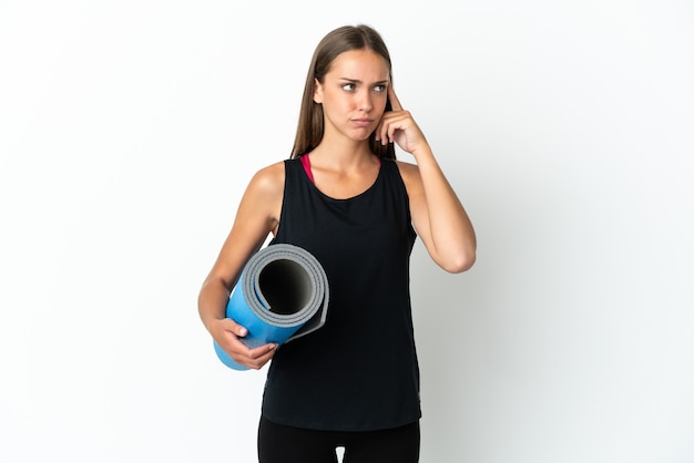 Sport woman going to yoga classes while holding a mat over isolated white background having doubts and thinking