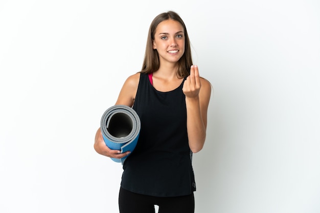 Sport woman going to yoga classes while holding a mat over isolated white background making money gesture