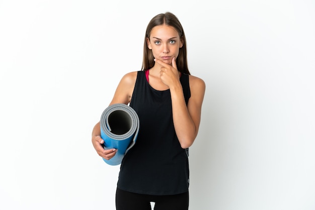 Sport woman going to yoga classes while holding a mat over isolated white background thinking