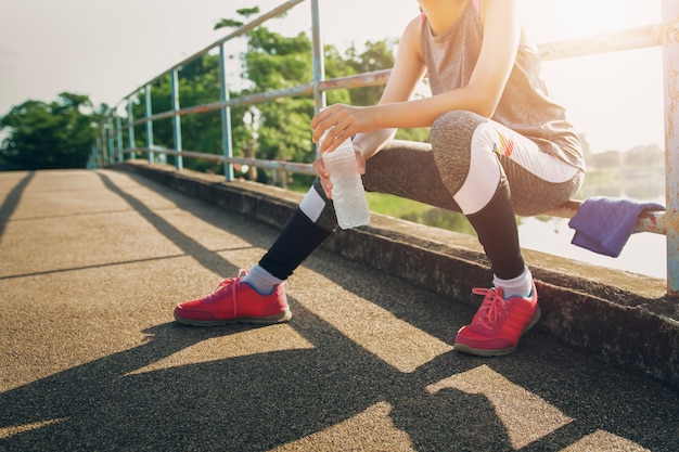 Donna di sport che si siede dopo avere funzionato con la bevanda della bottiglia di acqua della tenuta