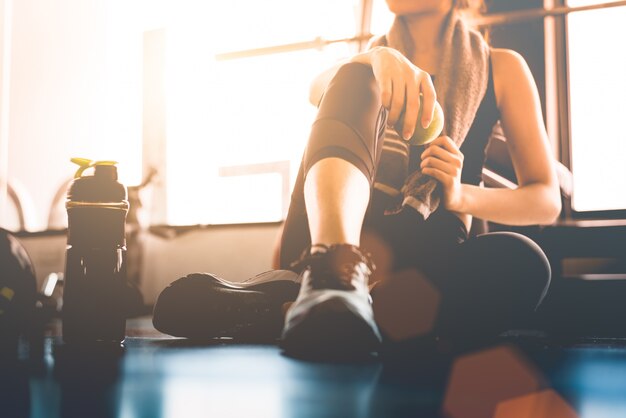 Metta in mostra la donna che si siede e che riposa dopo l'allenamento o l'esercizio nella palestra di forma fisica con il frullato di proteine