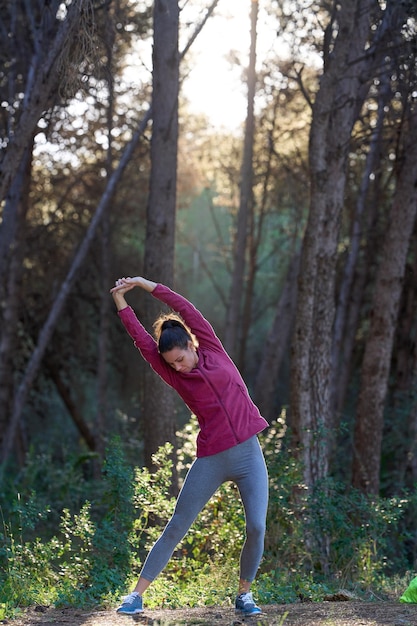 Foto donna sportiva che allunga il corpo nella foresta con raggio di sole e copia spazio