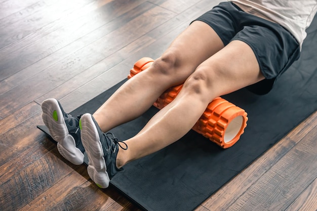 Спортсменка, использующая пенный валик для растяжки мышц и фасции ноги