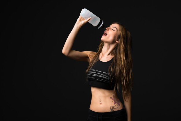 Sport woman with a bottle of water on dark background