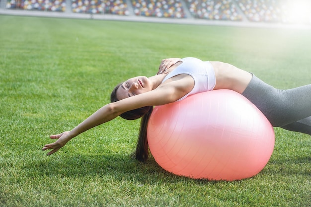Sport woman with fitball exercising outdoors on green grass