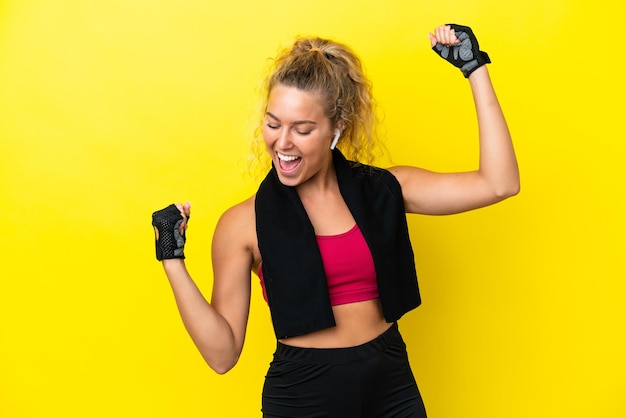 Sport woman with towel isolated on yellow background celebrating a victory