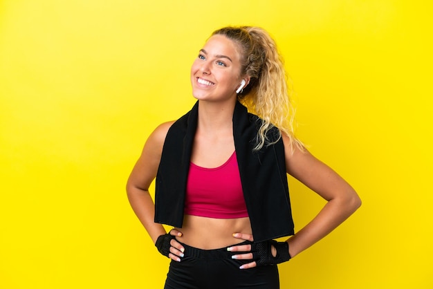 Sport woman with towel isolated on yellow background posing with arms at hip and smiling