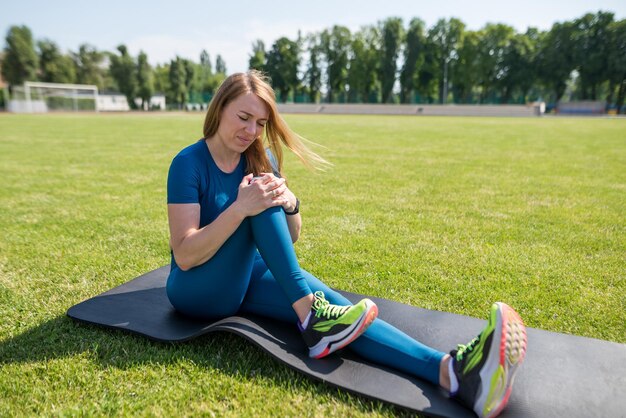 Sportblessure van de knie Een vrouw ervaart pijn in haar knie tijdens het sporten in een sportstadion-gezondheidsconcept