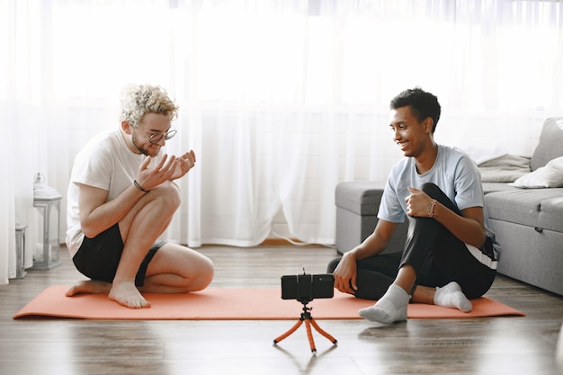 Foto sporten en gezond leven. fitnesstrainer en stagiair praten op fitness mat. de mannen zitten op de grond en filmen blog.