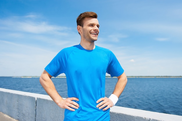 Sporten is zijn leven. Knappe jonge man in sportkleding hand in hand op heup terwijl hij buiten staat