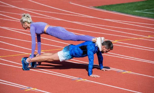 Foto sportfitness man en vrouw die samen trainen staan in de plank en duwen omhoog op de buitenrenbaan van het stadion met sportkleding, een gezonde levensstijl.