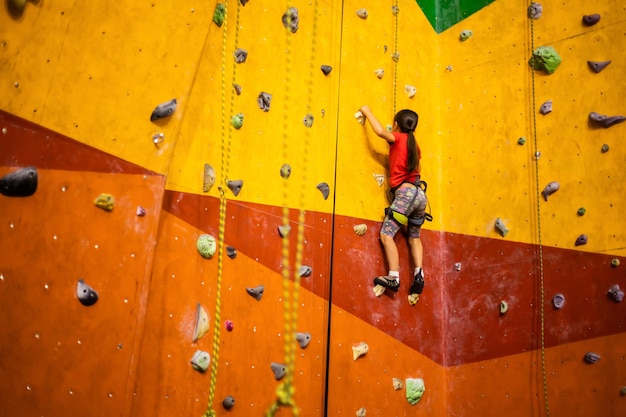 Sportief meisje kunstmatige rots klimmen op praktische muur in de sportschool