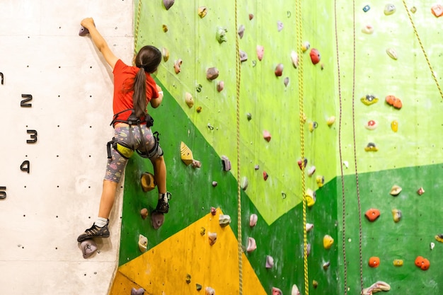 Sportief meisje kunstmatige rots klimmen op praktische muur in de sportschool