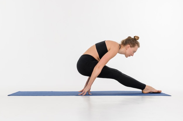 Sportieve aantrekkelijke jonge vrouw die yogapraktijk op witte achtergrond doet.