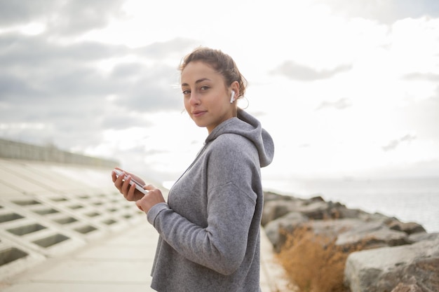 Sportieve aantrekkelijke vrouw die smartphone gebruikt en buiten naar muziek luistert in een koptelefoon