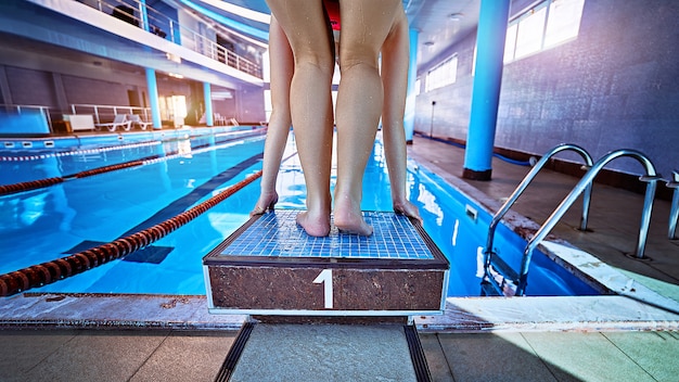 Sportieve atletische vrouwelijke kampioenenzwemmer in lage positie op startblok in een zwembad