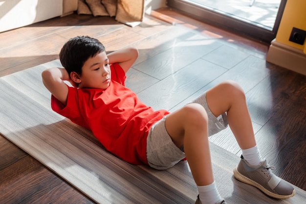 Sportieve aziatische jongen doet thuis buikspieren op fitnessmat tijdens quarantaine