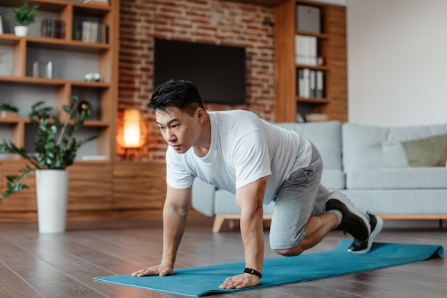 Sportieve aziatische man van middelbare leeftijd die lopende plankoefening doet op yogamat thuis in de kopieerruimte van de woonkamer