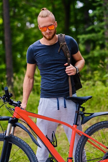 Sportieve bebaarde man zit op een rode bergfiets buiten.