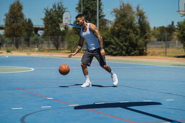 Sportieve blanke man met coole tatoeages die basketbal speelt op het buitenveld