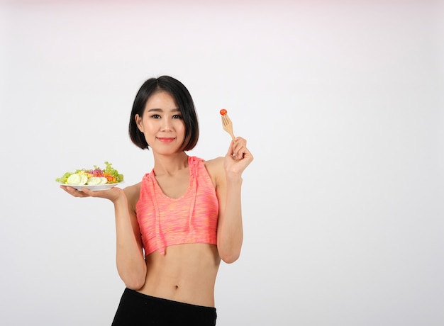 Sportieve fitness vrouw in sportkleding met plantaardige salade op wit