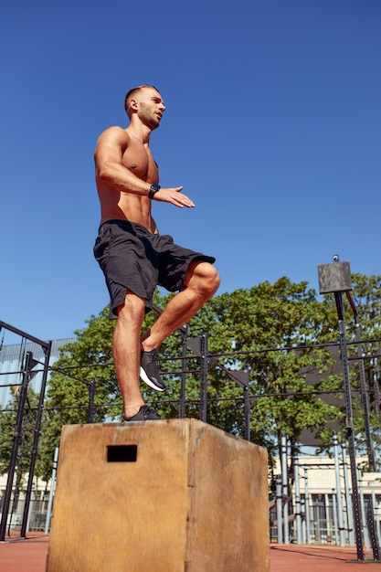 Sportieve fysiek fitte man doet step-up oefening op houten kist terwijl hij buiten gym traint