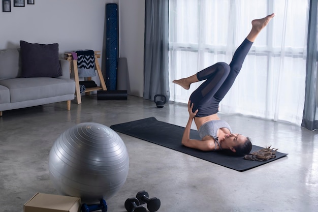 Sportieve jonge Aziatische vrouw die yoga doet in de woonkamer Jonge vrouw in sportkleding die thuis traint en kijkt naar online fitnesslessen in de woonkamer