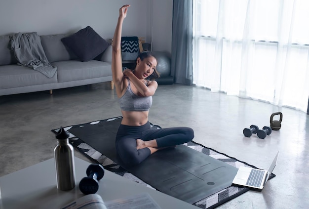 Sportieve jonge Aziatische vrouw in sportkleding die thuis traint om fitnessvideo op internet te kijken of online fitnessles te hebben met behulp van laptop woonkamer interieur kopieerruimte