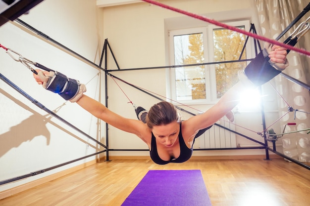 Sportieve jonge kaukasische vrouw die rekoefeningen doet van volledige lichaamsspieren trainen op stretch aerobic aero strap in gymyogi mat