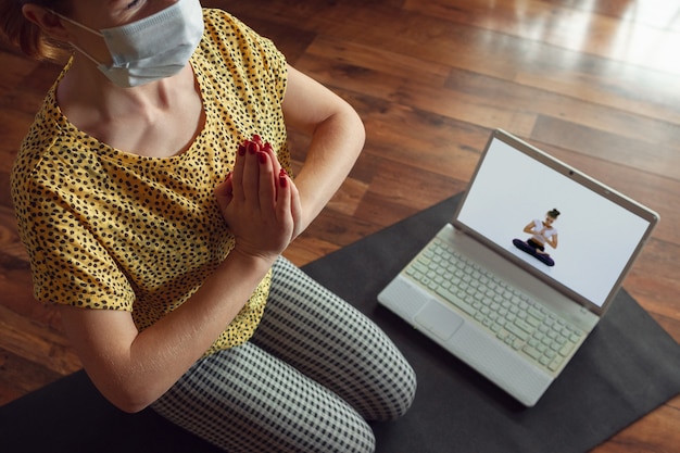 Sportieve jonge vrouw die online yogalessen volgt en thuis oefent terwijl ze in quarantaine is. concept van een gezonde levensstijl, wellness, veilig zijn tijdens een pandemie van het coronavirus, op zoek naar een nieuwe hobby.