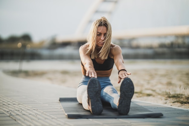 Sportieve jonge vrouw die rekoefeningen doet tijdens het opwarmen voor sporttraining buiten.