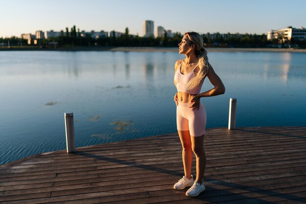 Sportieve jonge vrouw die traint en de nek uitrekt om op te warmen voordat ze gaat rennen of trainen in de buurt van water op de achtergrond van het stadsbeeld